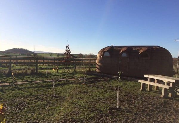 iglu glamping hut view from outside with grass, table and blue sky