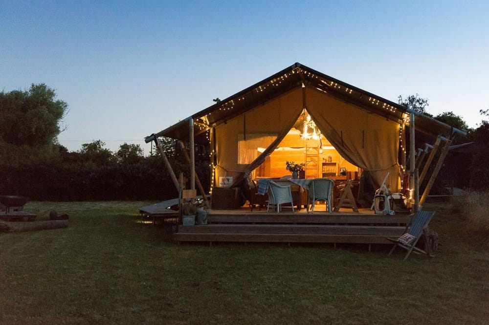 upsticks Glamping tents in the UK view from the outside with a deck, lights and dusk sky in the backgorund