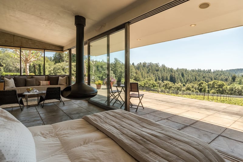 Vineyard Glamping Bay Area retreat view from inside with bed and couch and fireplace with patio and a vineyard view out the glass walls