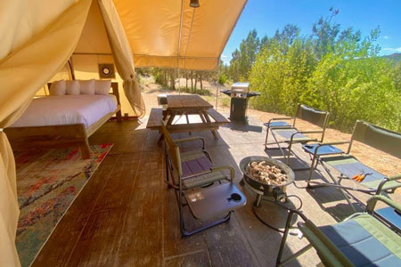 Top Glamping in Zion National Park to Love 11 view from east zion glamping tent deck with door open and bed inside and chairs, picnic table, bbq and firepit on the deck